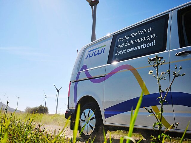 Servicefahrzeug von JUWI fährt auf einem Feldweg. Im Hintergrund sind Windräder zu sehen.