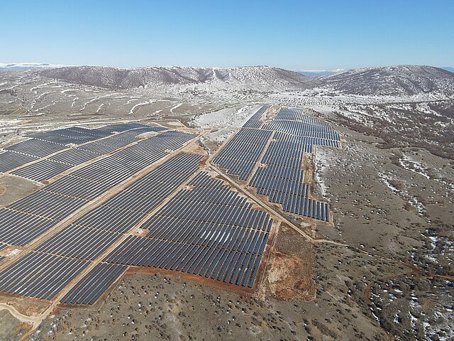 Ein großer Solarpark im Winter. Leichter Schnee ist auf den Hügeln im Hintergrund des Parks zu erkennen. 