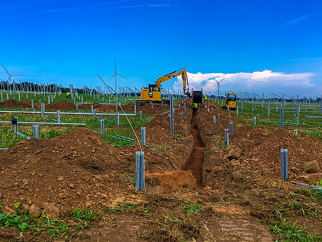 Mit einem Bagger werden Kabeltrassen in einem Solarpark verlegt.