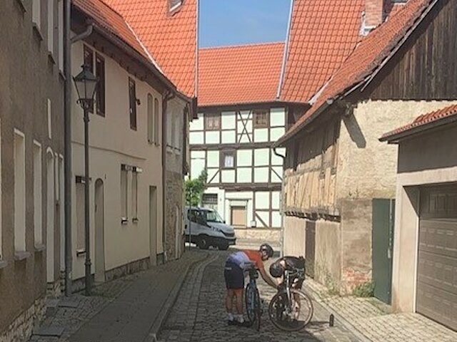 Zwei Radler stehen in einer engen Gasse und flicken eine Reifen.