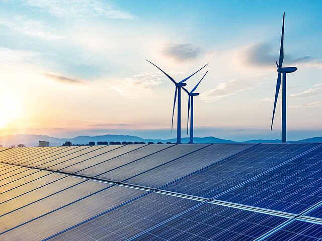 Hinter einer Solaranlagen ragen zwei Windenergie-Anlagen in die Höhe.
