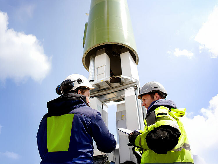 Zwei Mitarbeiter stehen vor einer Windenergie-Anlage, die gerade montiert wird. 