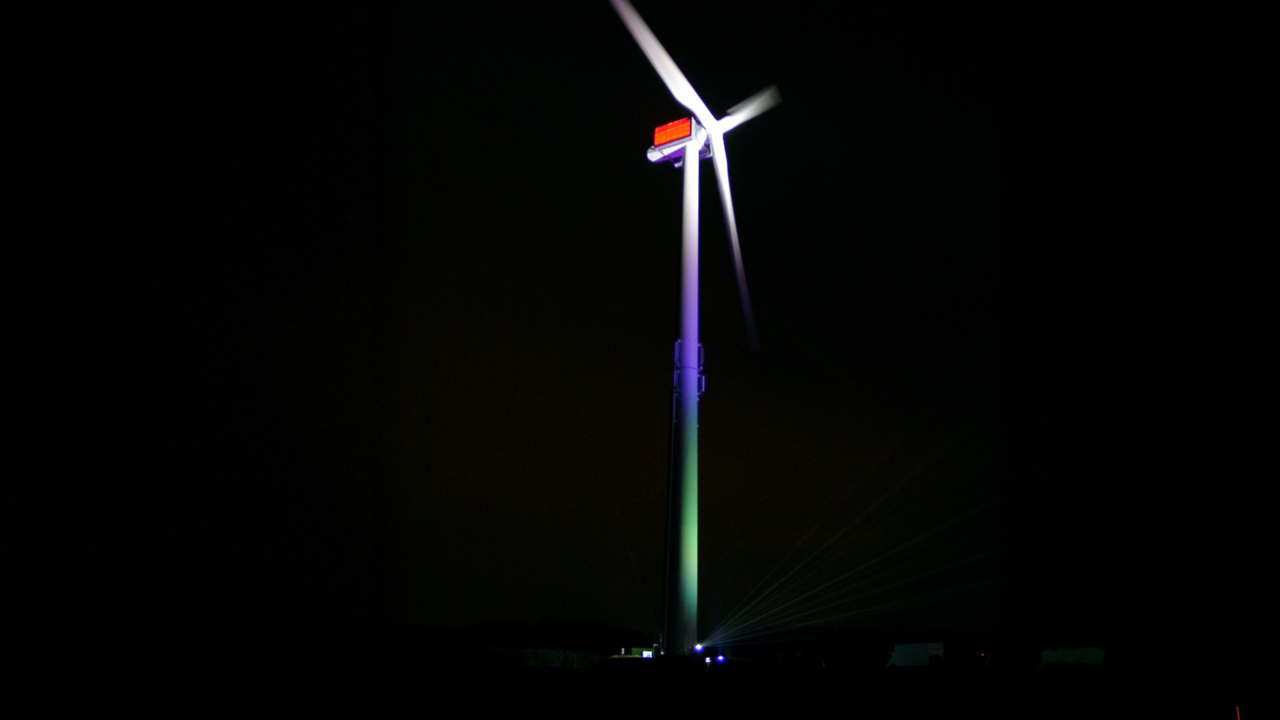 Die gesamte Windenergie-Anlage bunt beleuchtet im Dunkeln.