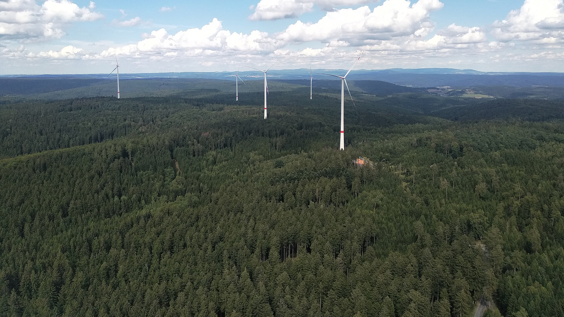 Windkraftanlagen im grünen Wald aus der Vogelperspektive. Der Himmel ist leicht bewölkt.