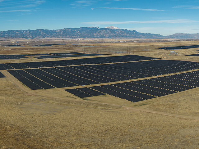 Foto des Pike Solar Parks in Colorado. Hinter dem gewaltigen Solarprks erheben sich majestätisch Berge in den blauen Himmel.
