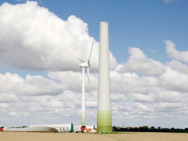 Der Stumpf eines Turms streckt sich in die Höhe. Daneben liegen weitere Bauteile einer Windenergie-Anlage.