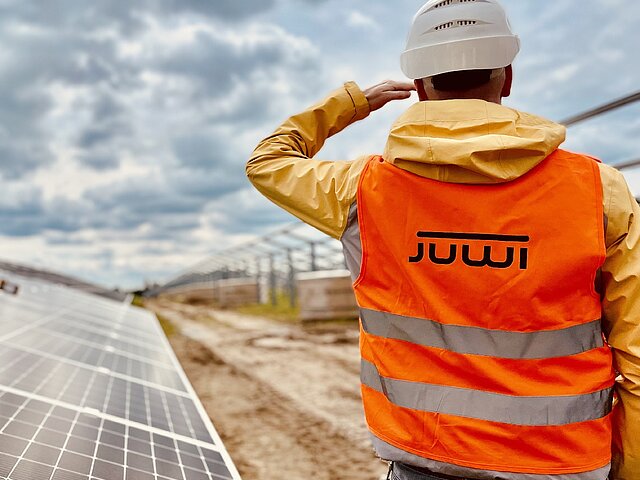 Ein JUWI-Mitarbeiter mit Warnweste steht auf einer PV-Baustelle und überwacht die Arbeiten.