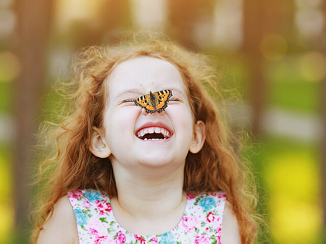 Ein Kind lacht und hat einen Schmetterling auf der Nase sitzen