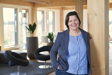 Sabrina Petersen lehnt an einem Holzpfeiler und lächelt in die Kamera.