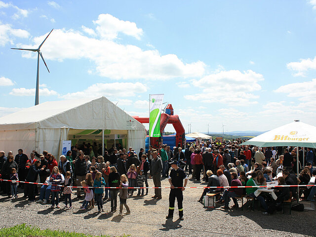 Windparkfest am Windrad mit Zelten, vielen Besuchern und einem Windrad im Hintergrund.