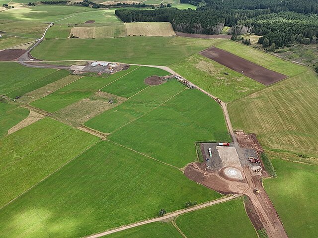 Auf einem grünen Feld sind die Vorbereitungen für eine Windenergieanlage zu sehen.