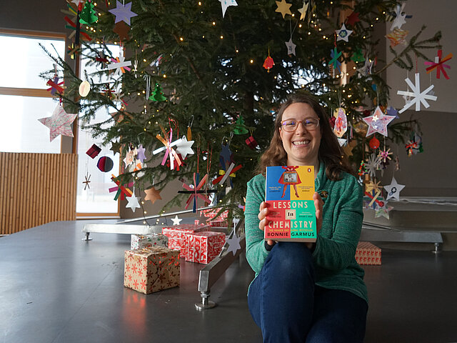 Tanja Sonntag sitzt vor einem Weihnachtsbaum und hält ihren Lesetipp in die Kamera. 