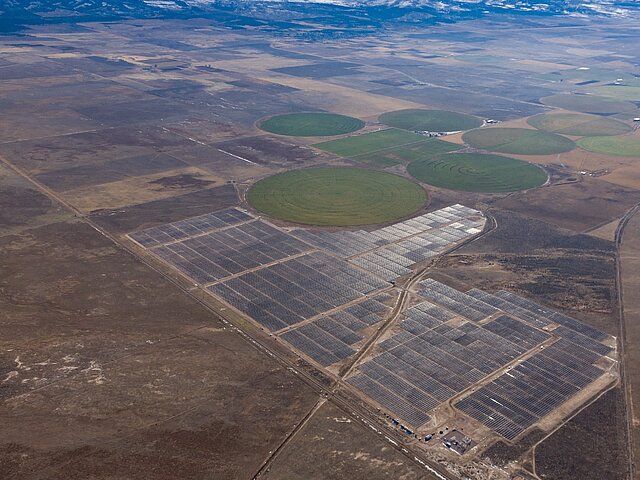 Der Solarpark Pavant, der sich in Mitten der weiten Ebenen in Utah befindet. An seinem Rand sind landwirtschaftlich genutzte, kreisförmige Flächen zu sehen.