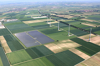 Mehrere Windenergie-Anlagen stehen auf landwirtschaftlich genutzten Flächen, in direkter Nachbarschaft steht ein Solarpark.  