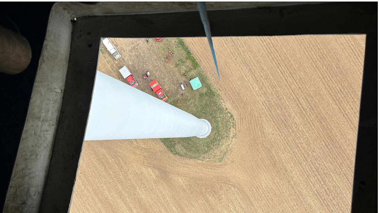Perspektive aus der Kranluke einer Windenergieanlage auf ein Feld mit Rettungsfahrzeugen hinab.