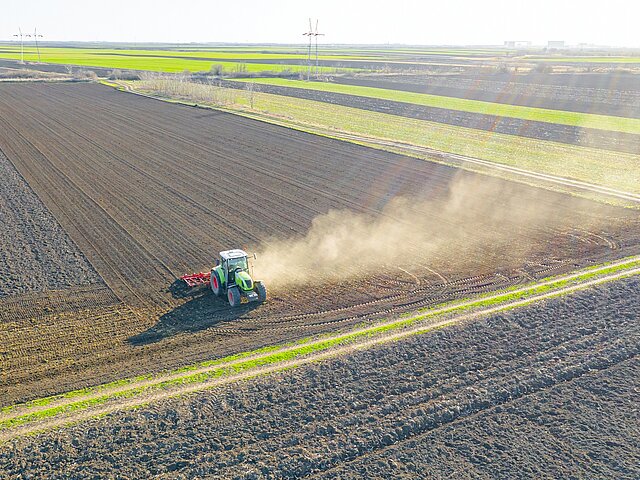 Ein Traktor arbeitet auf einem Feld, viel Staub wird dabei aufgewirbelt.