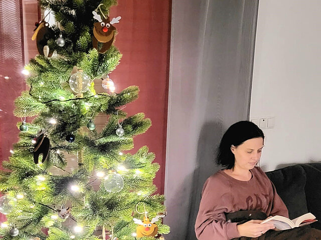 Stefanie Heidrich sitzt neben einem geschmückten Weihnachtsbaum und liest eine Buch.
