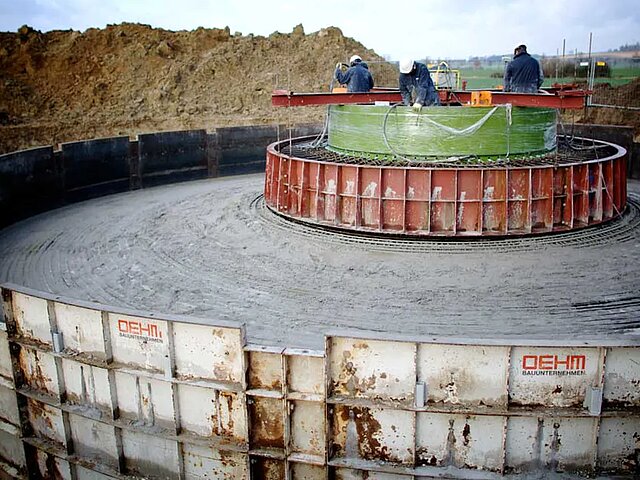 Mehrere Arbeiter stehen auf dem Betonfundament und arbeiten.