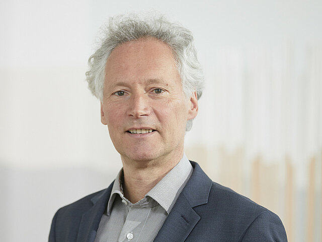 Lothar Schulze steht vor einer weißen Wand und lächelt in die Kamera