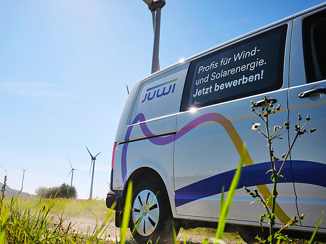 Ein Transporter mit JUWI-Logo steht in einem Windrad. Die Sonne scheint.