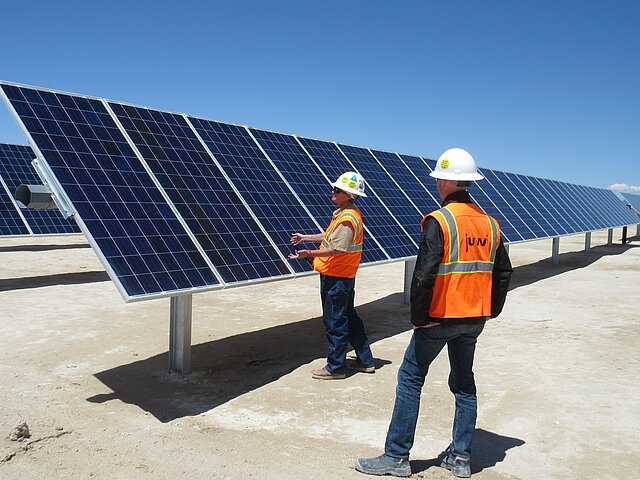 Zwei JUWI-Ingenieure arbeiten am Solarparkbei strahlendem Sonnenschein.
