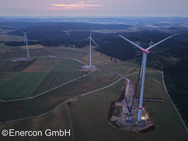 Drei Windenergieanlagen auf einem großen Feld in der Abenddämmerung.