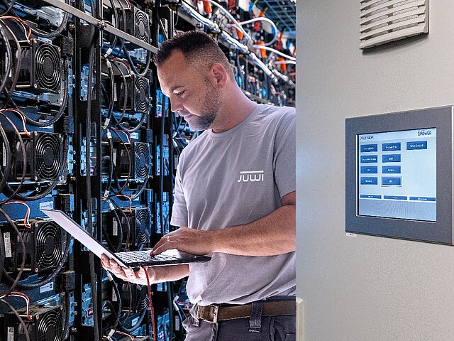 Ein JUWI-Mitarbeiter steht liest Daten mit hilfe eines Laptops aus.