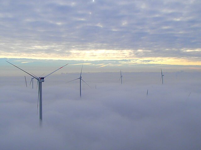 Eine Windenergie-Anlage ragt über eine dichte Wolkendecke hinaus.
