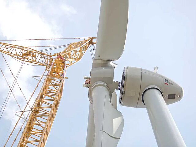 Ein großer Kran hebt die Rotorblätter einer Anlage zur Gondel, wo sie montiert werden müsssen.