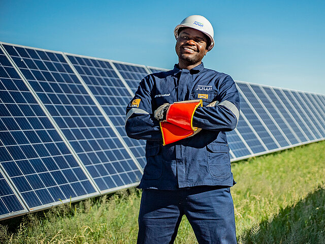 Ein JUWi-Techniker steht vor einer langen Reihe Solarmodule und lächelt in die Kamera.