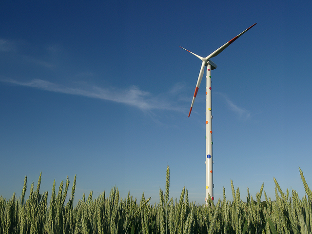 Windenergieanlage mit bunten Punkten auf einem Feld vor blauem Himmel.