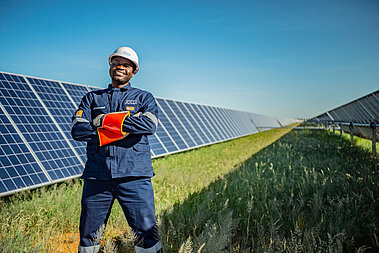 Ein JUWi-Techniker steht vor einer langen Reihe Solarmodule und lächelt in die Kamera.