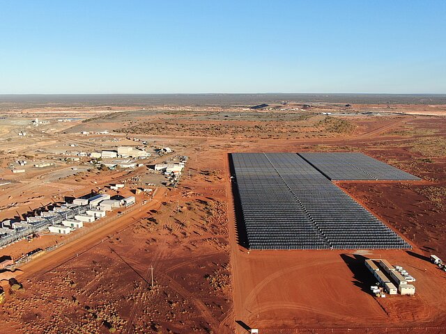 Im Vordergrund ist die Solaranlage für die Agnew-Goldmine in Australien zu sehen. Die blauen Paneele bilden einen starken Kontrast zum orangefarbenen Boden des australischen Outbacks.