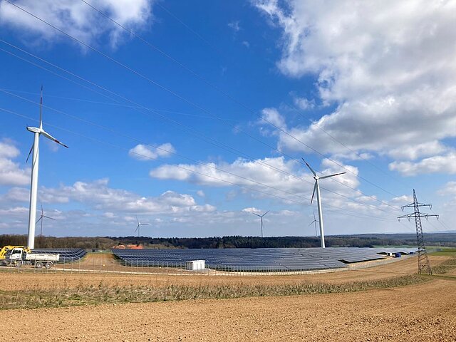 Im Vordergrund ist ein Solarpark und im Hintergrund sind Windräder zu sehen.