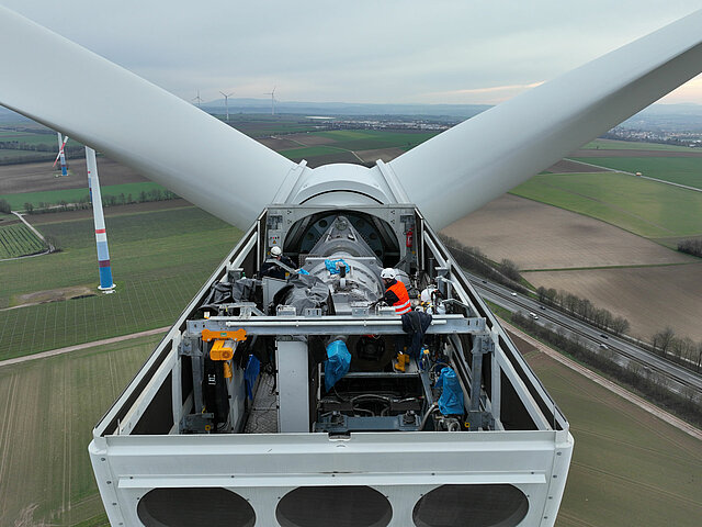 JUWI-Mitarbeitende bei Arbeiten an der Turbine in der Gondel. Das Dach wurde entfernt. Das Bild zeigt in welchen schwindelerregnenden Höhen die Arbeiten durchgeführt werden.