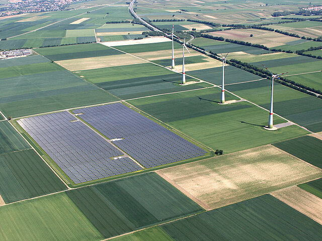 Mehrere Windenergie-Anlagen stehen auf landwirtschaftlich genutzten Flächen, in direkter Nachbarschaft steht ein Solarpark.  