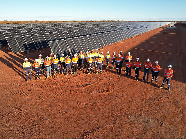 Several construction workers are standing proudly in front of the completed solar park.