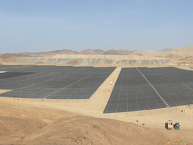Solarpark der Mine in Ägypten. Im Hintergrund sind Berge und Geröllaufschüttungen zu erkennen. Die Sonne scheint auf die langen Reihen von schwarzen Photovoltaik-Anlagen.
