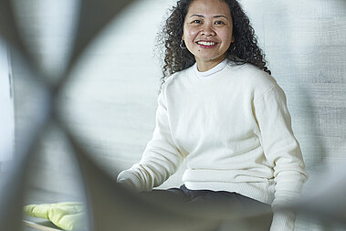Beverly sitzt auf einer Bank und lächelt in die Kamera.