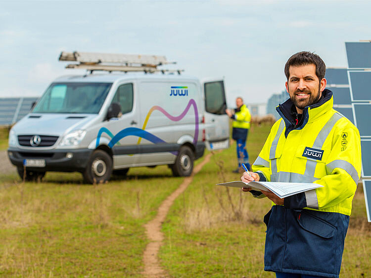 Ein JUWI-Mitarbeiter steht in einem Solarpark und schaut auf ein Klemmbrett. 