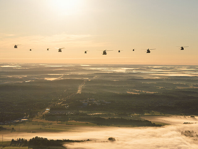 Eine Gruppe Helikopter der Bundeswehr fliegt auf die Kamera zu.. Die Sonne geht langsam unter.