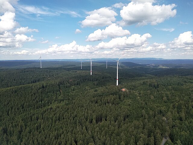 Windenergie-Anlagen im grünen Wald aus der Vogelperspektive. Der Himmel ist leicht Bewölkt.