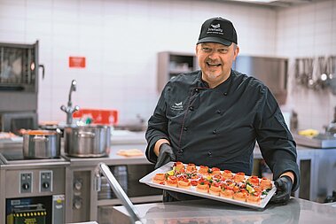 Kens Kottke steht in der Küche und lächelt in die Kamera.