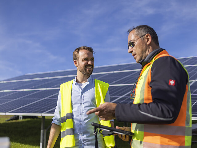 Zwei JUWI-Mitarbeiter stehen in einem Solarpark und diskutieren miteinander.