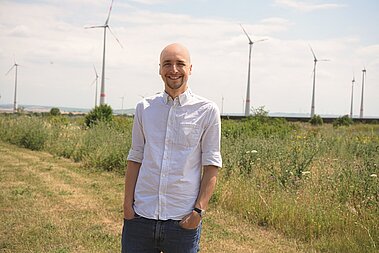 Doktor Manuel Gardt steht vor mehreren Windrädern.