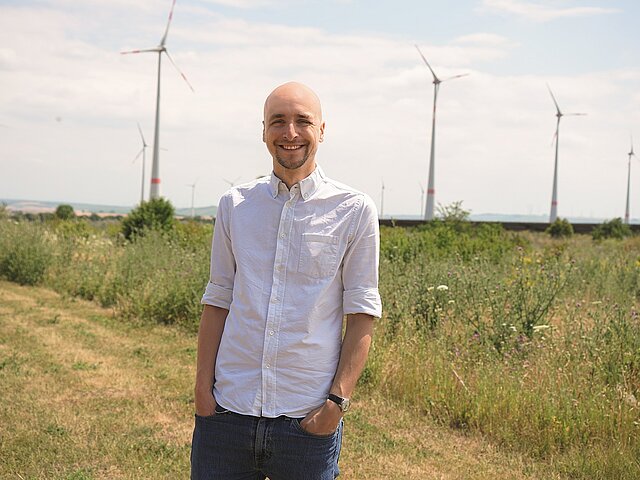 Doktor Manuel Gardt steht vor mehreren Windrädern.