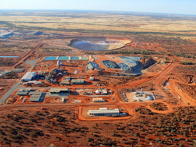 Ein Bild der Mine und der ihr angegliederten Gebäude aus der Vogelperspektive. Der rote Boden Australiens hebt sich deutlich ab. Im Hintergrund ist der Minenschaft erkennbar.