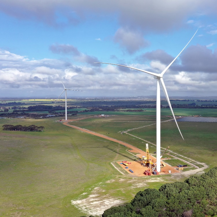 Zu sehen ist eine Windenergie-Anlage des Parks. An ihrem Fuß steht noch ein Kran, es werden letzte Arbeiten verrichtet. Im Hintergrund ist ein Teil des Solarparks zu sehen.